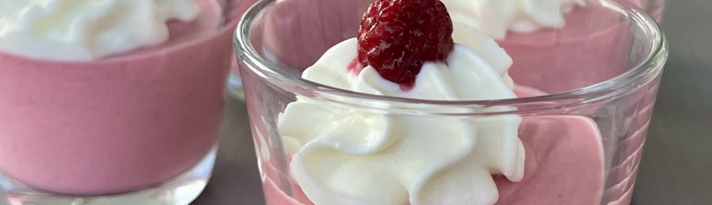 Glas med hallonmousse toppad med vispad grädde och hallon