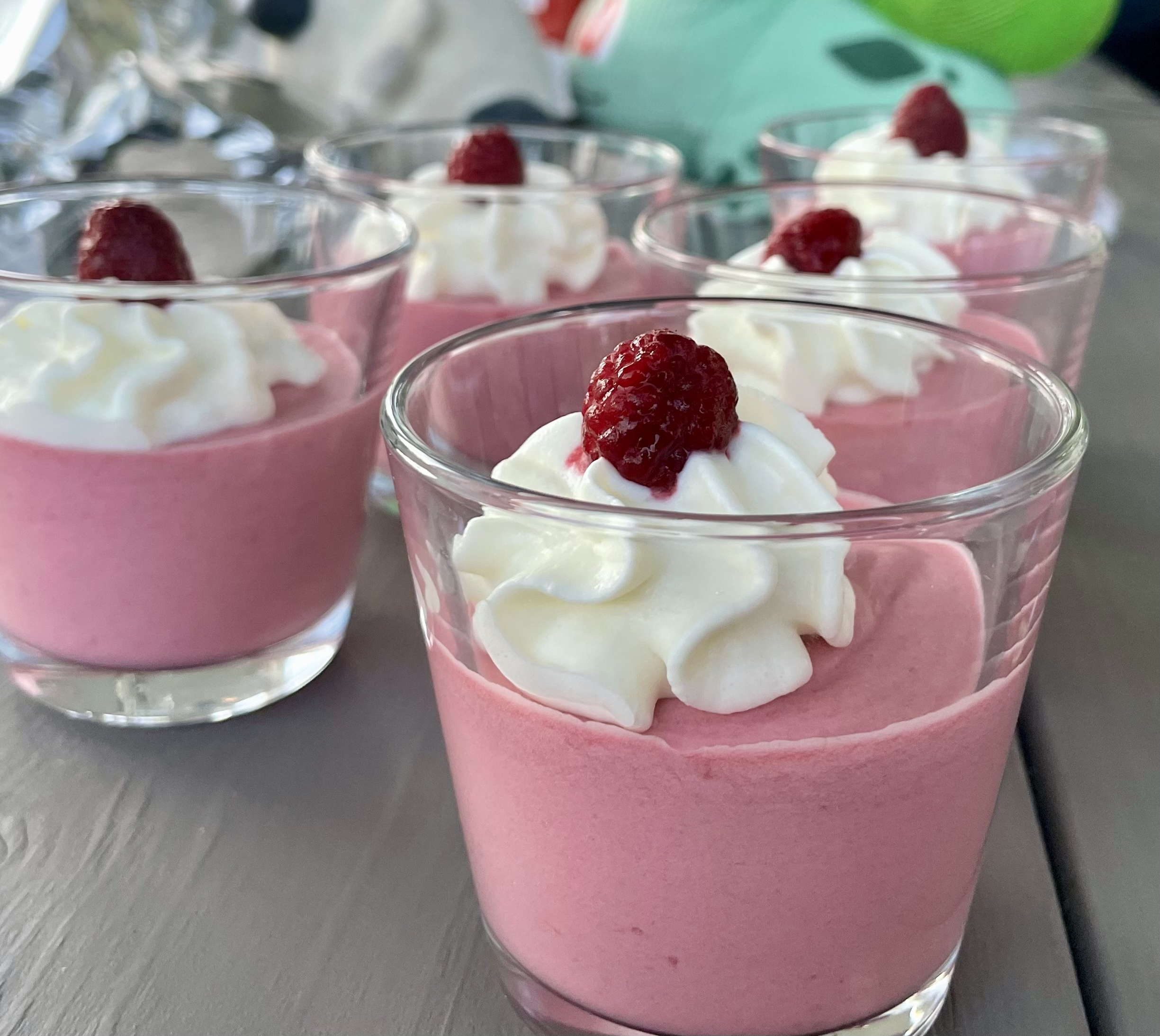Glas med hallonmousse toppad med vispad grädde och hallon